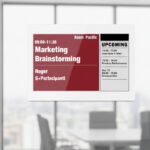 Un display E-Ink montato sulla parete di vetro di una sala riunioni moderna, che mostra lo stato di occupazione.